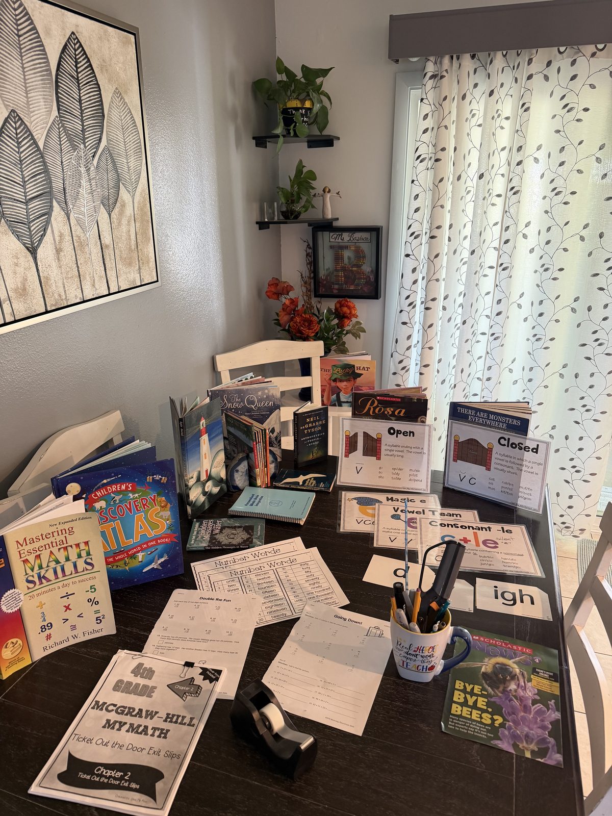 Tutoring table in Ms. Bastian’s house, set with math workbooks, children’s books, and phonics cards